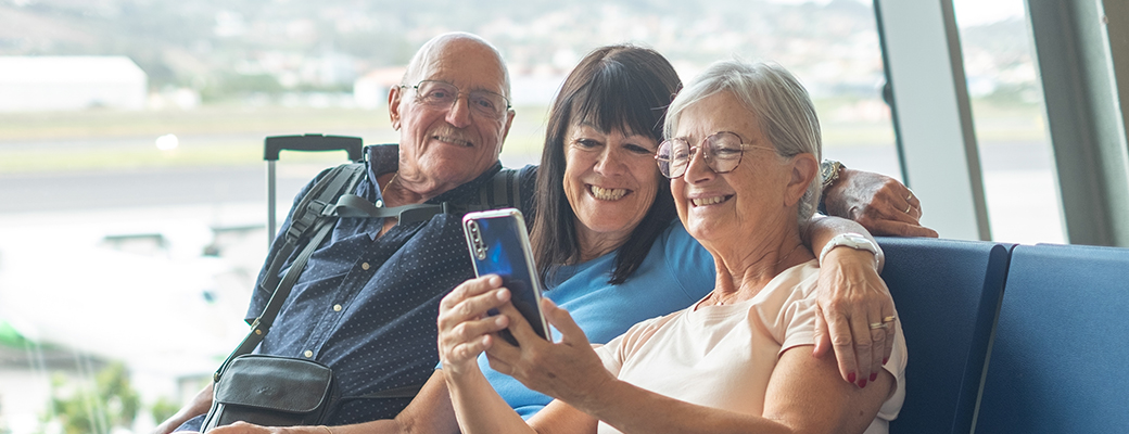 Image of two senior women and one senior man looking at a smartphone at an airport